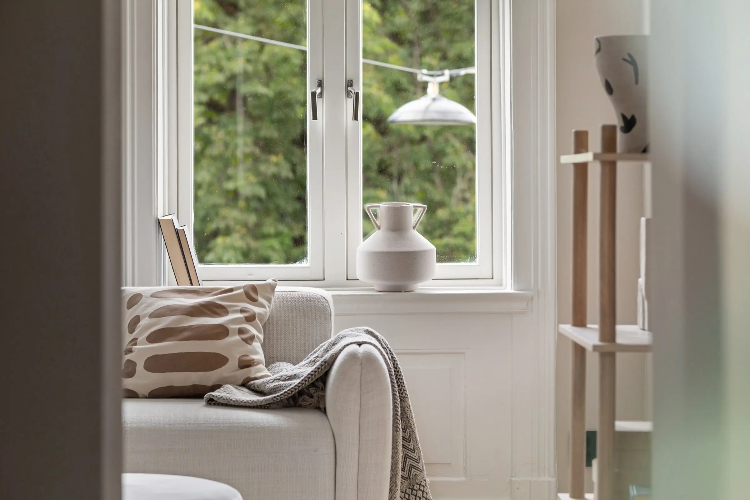 A calm living room with a sofa, a soft blanket and daylight from a large window