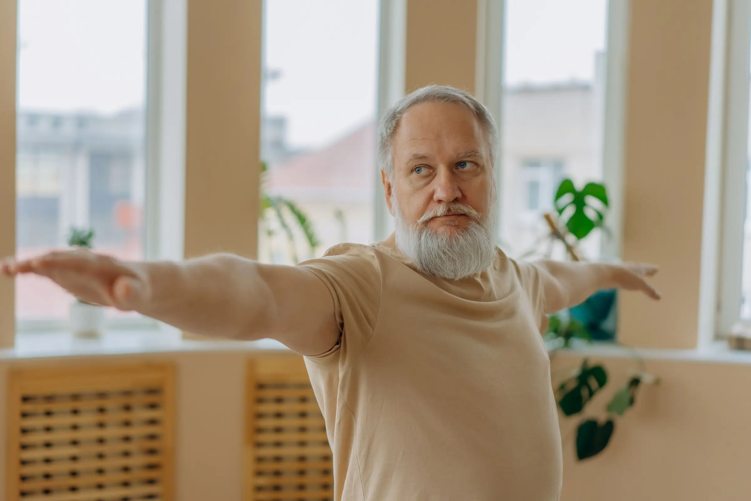 An older man standing with his arms held out to the sides in a bright living room