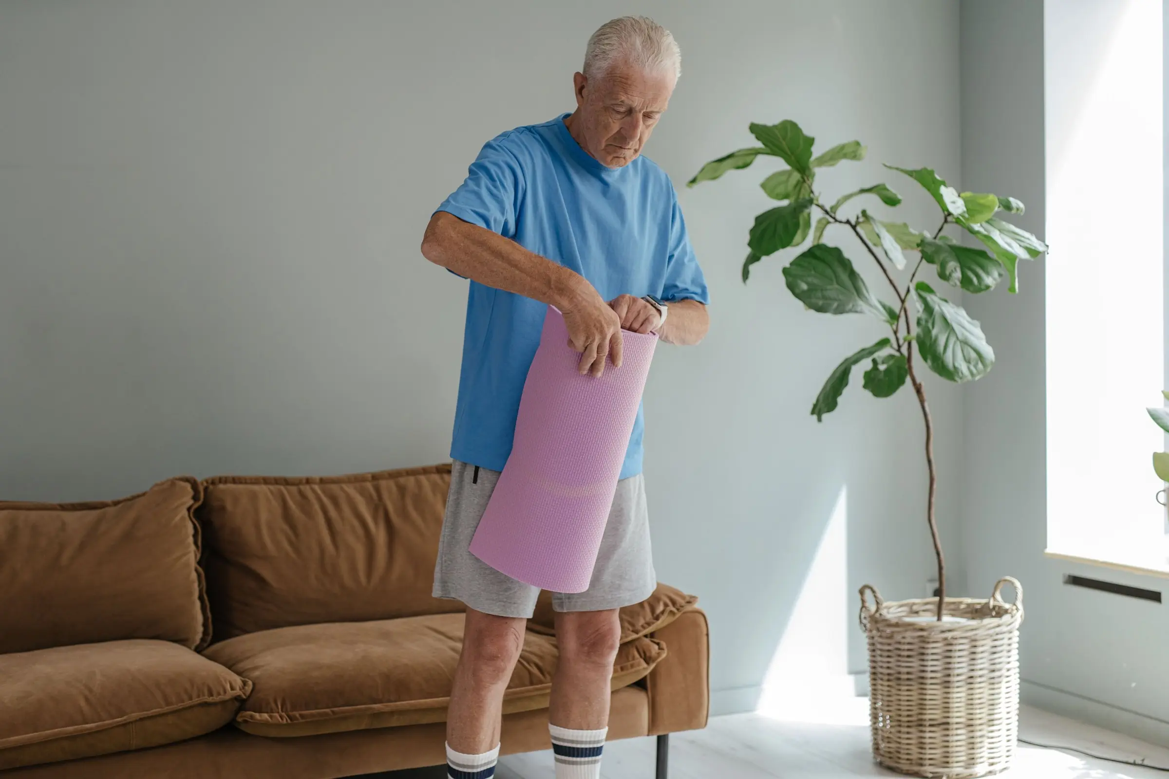 An older man unrolling an exercise mat in his living room