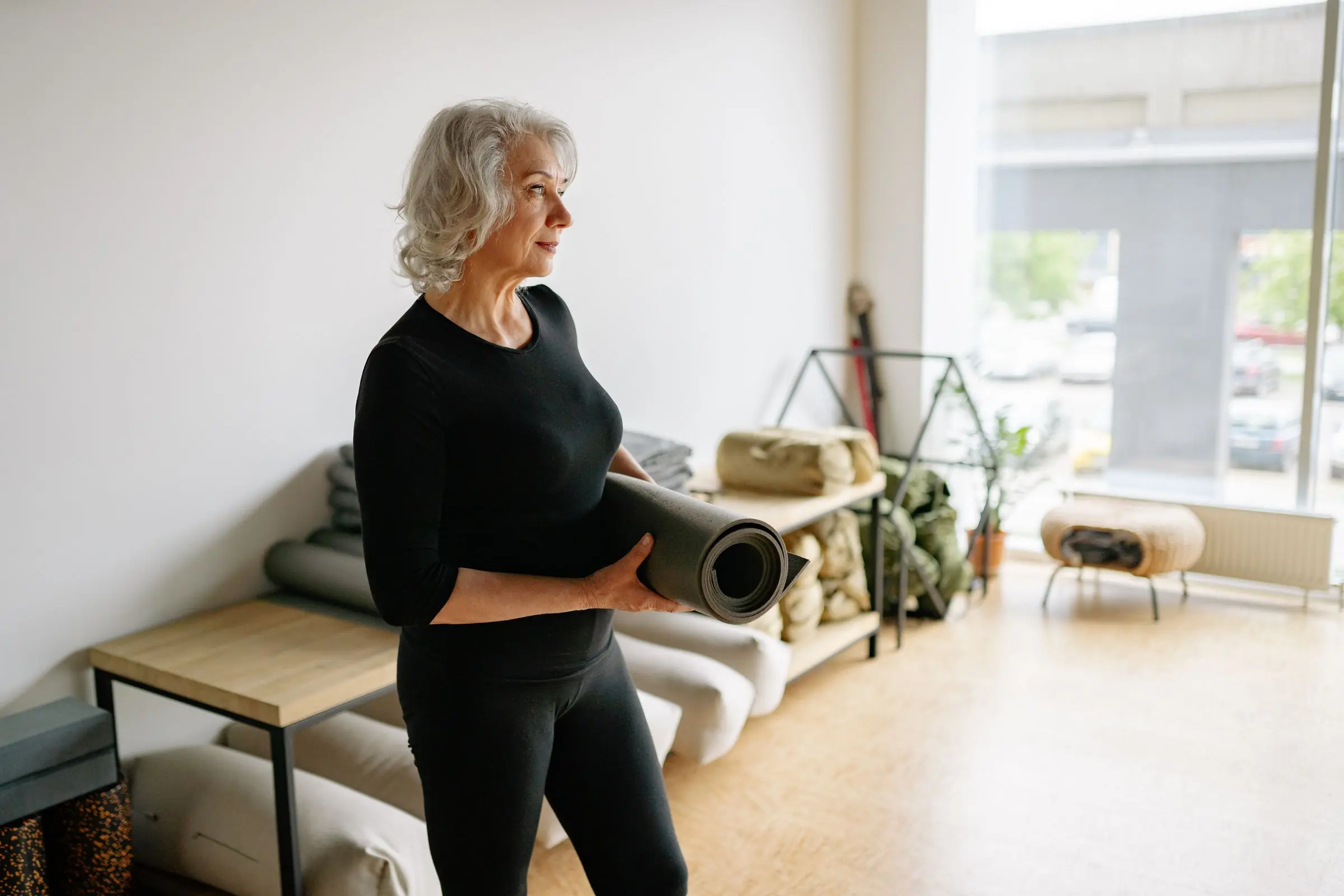 An older woman standing in her living room holding a rolled-up exercise mat