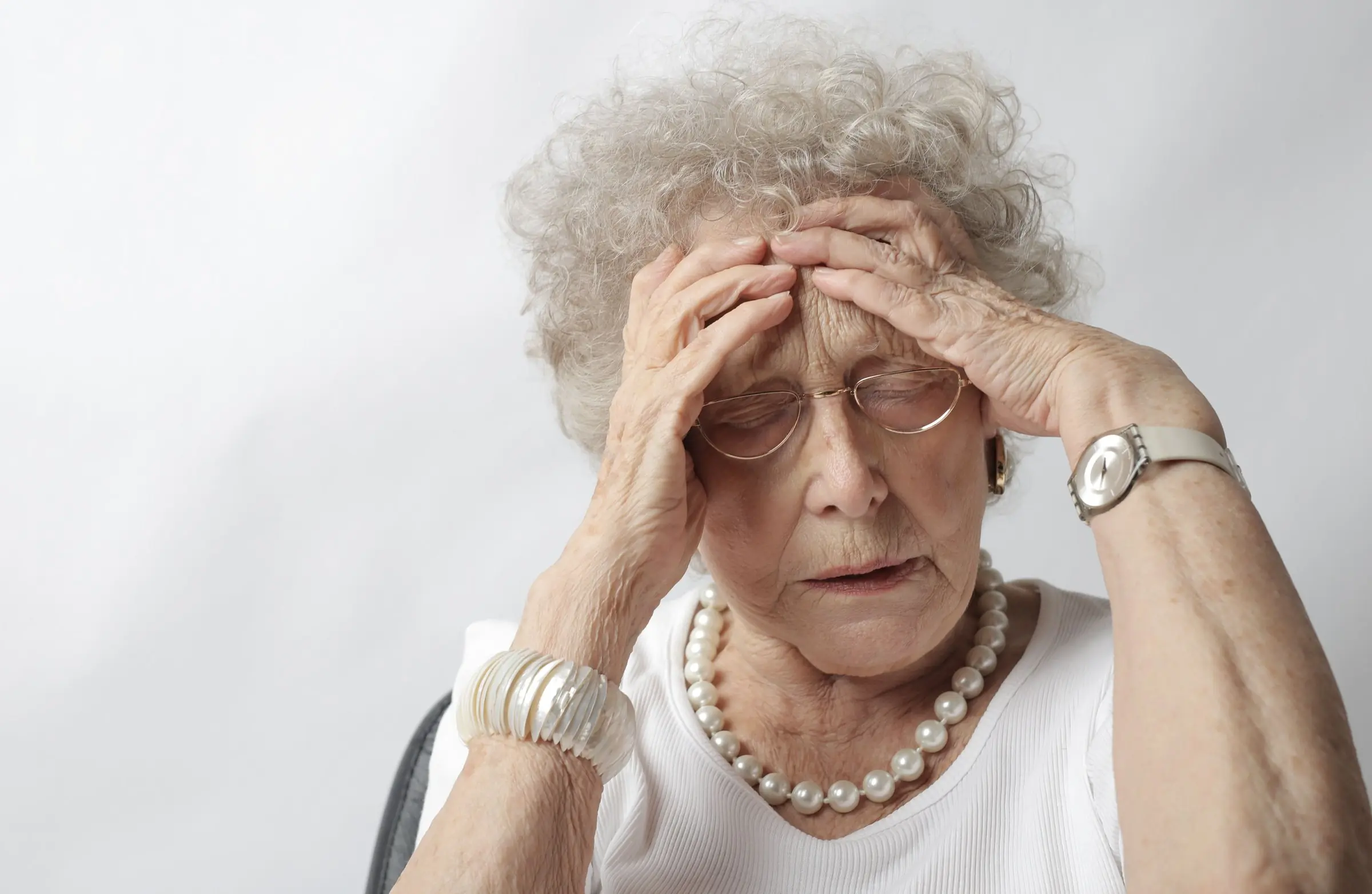 An older woman with her eyes closed and both hands pressed to her forehead
