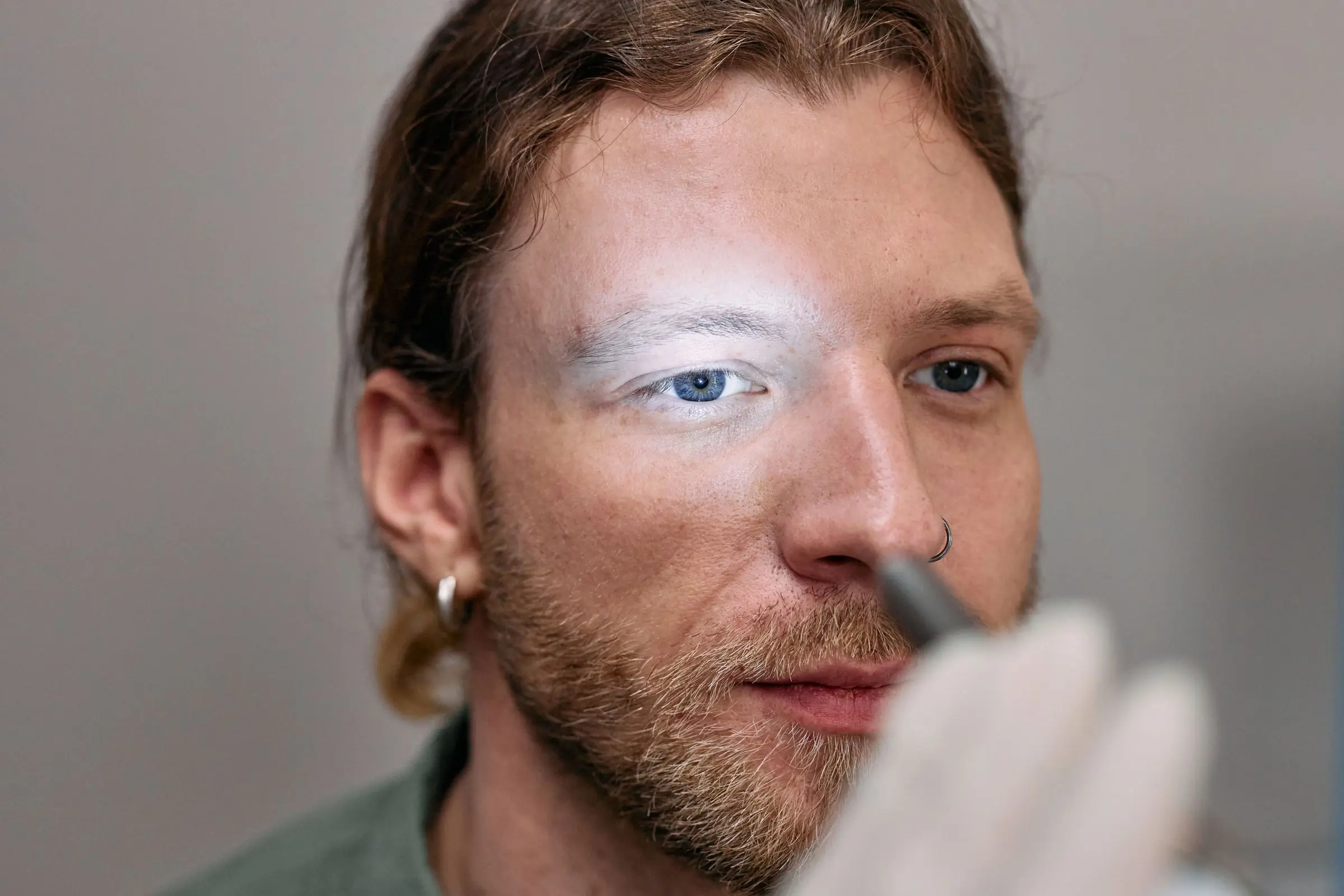 A man looking ahead while a gloved hand shines a small penlight towards his eyes