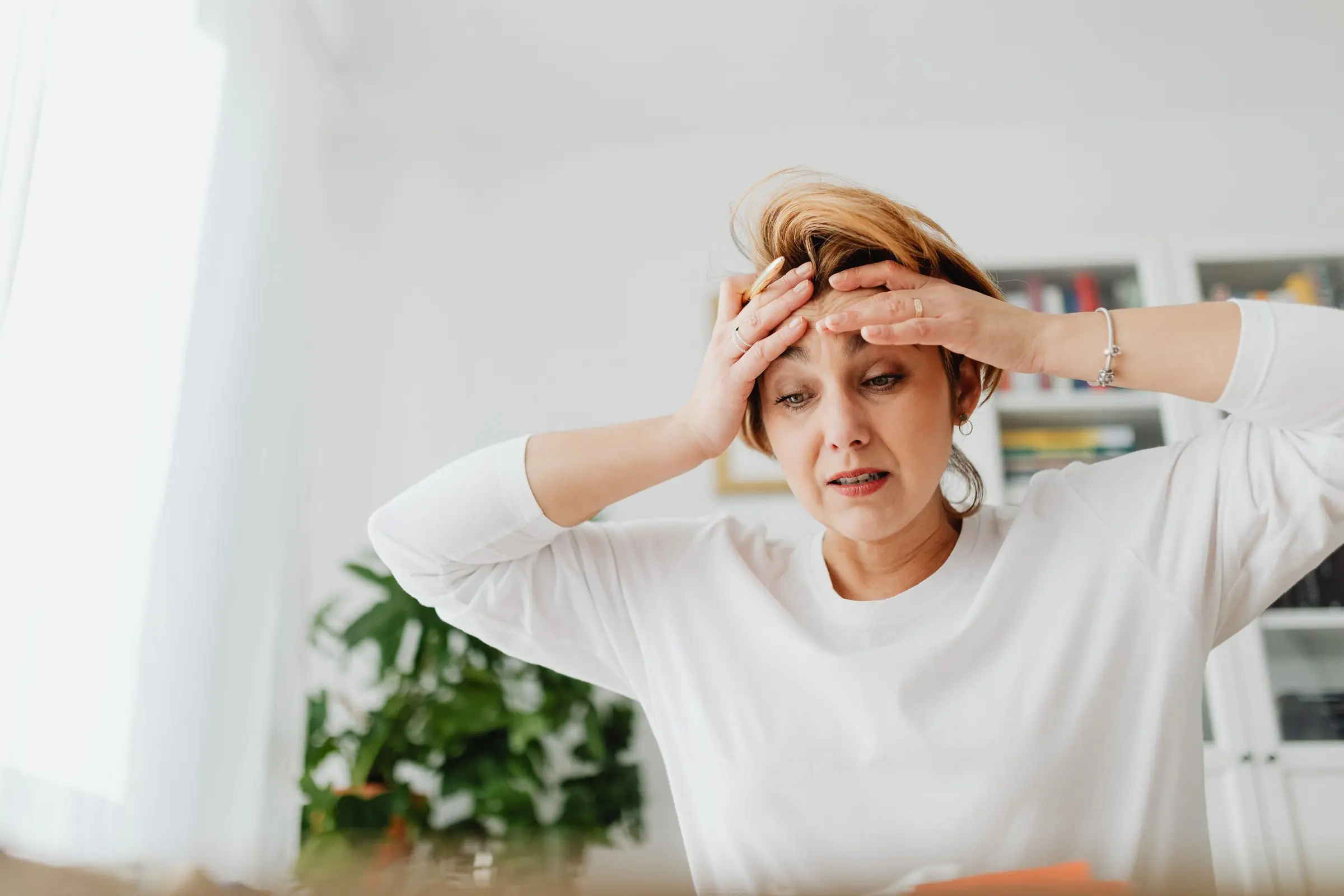 A woman standing in her home with both hands pressed to her forehead