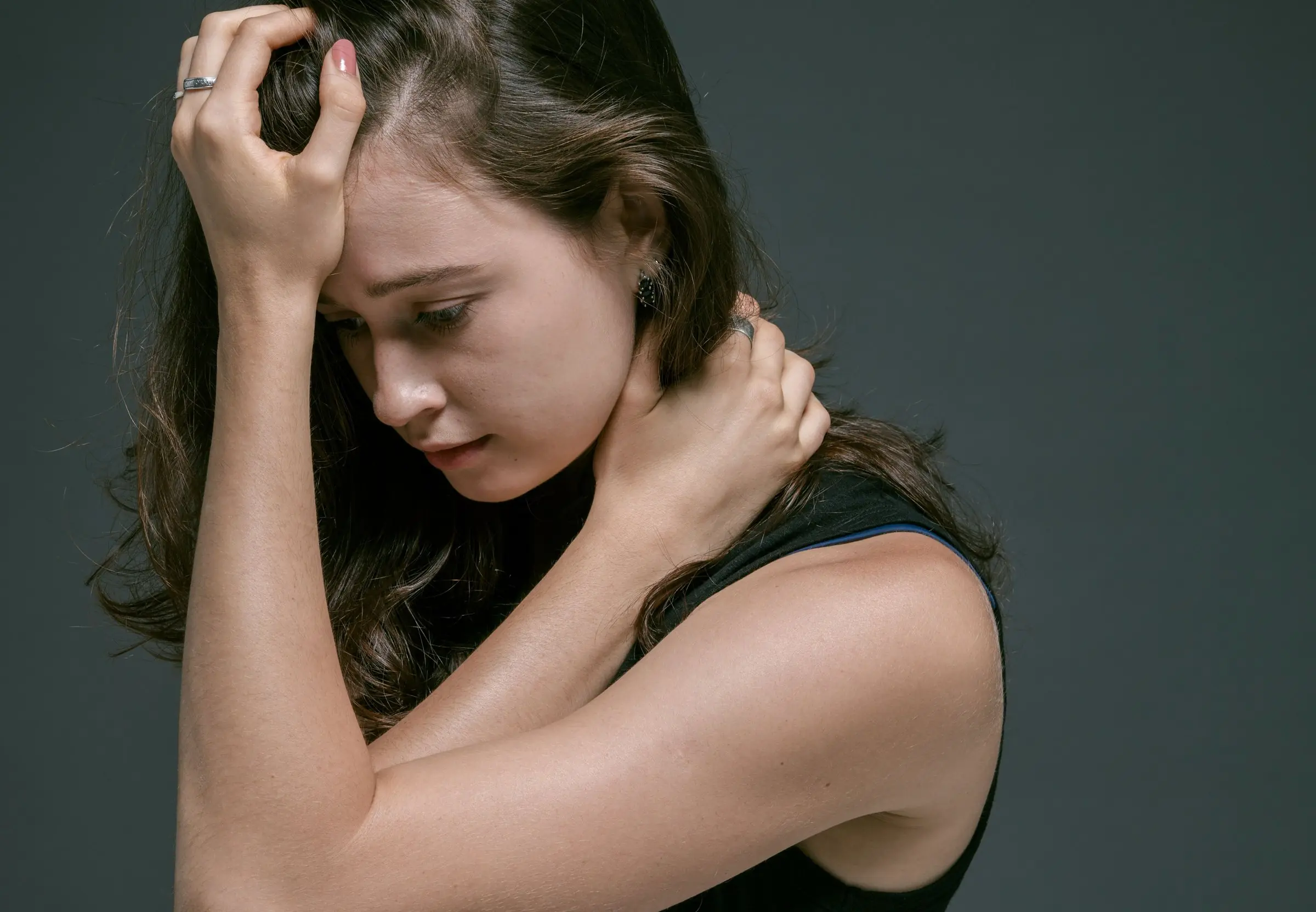 A woman with her eyes lowered, one hand on her forehead and the other on her neck